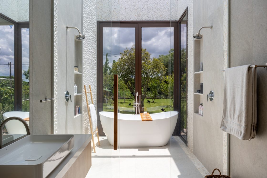 Banheiro em tons claros com banheira ofurô e janela ampla com vista para jardim