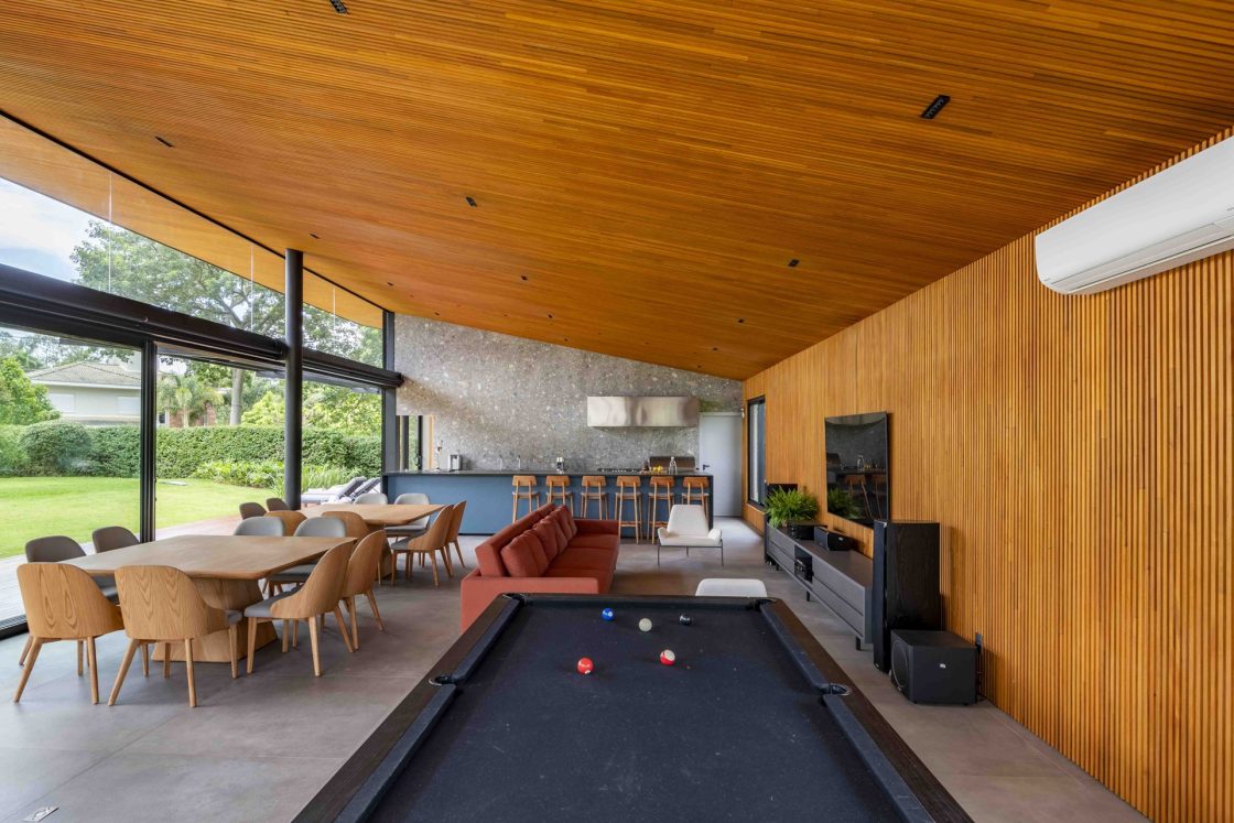 Espaço amplo que integra sala de jogos, área gourmet e sala de estar, com piso em porcelanato e teto forrado em madeira
