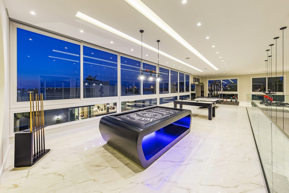 Sala de jogos ampla com parede de vidro e vista para o exterior à noite
