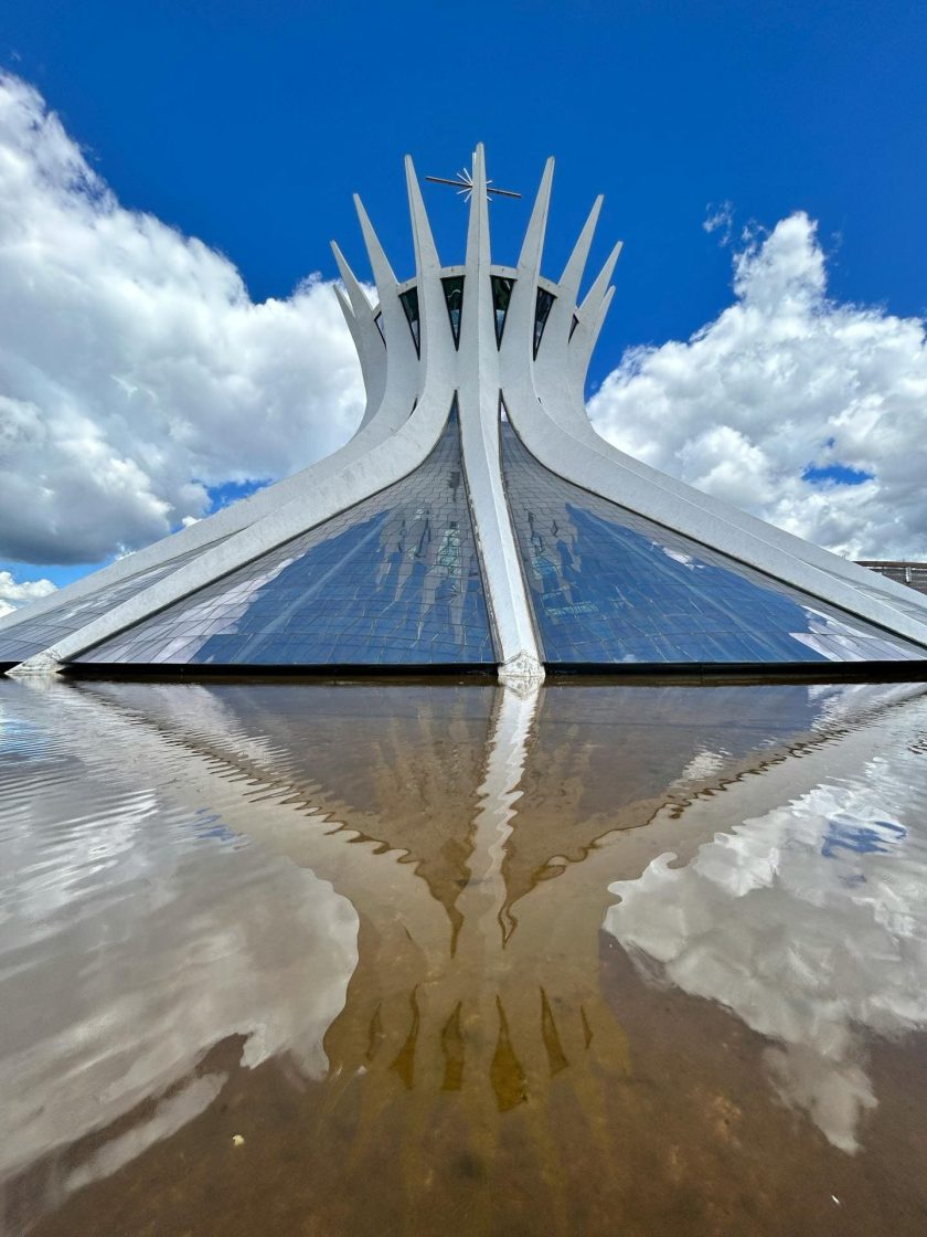 Catedral Metropolitana de Brasília vista de frente, com suas colunas curvas de concreto refletidas em um espelho d'água
