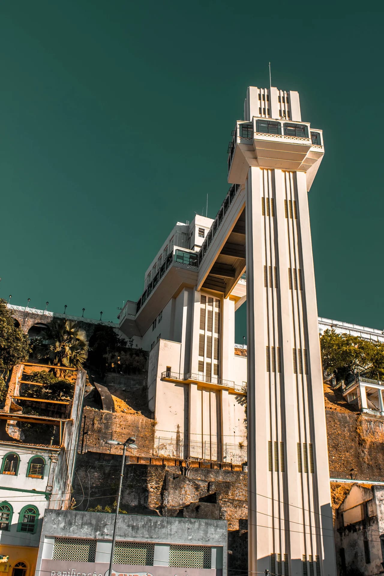 Vista de baixo para cima do Elevador Lacerda, em Salvador, destacando a torre vertical em estilo art déco e a passarela suspensa que conecta a Cidade Alta e a Cidade Baixa