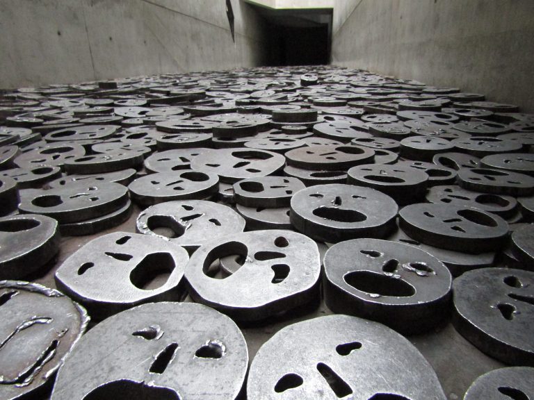 Rostos feitos com aço recobrem o chão todo e simulam massas de judeus em desespero