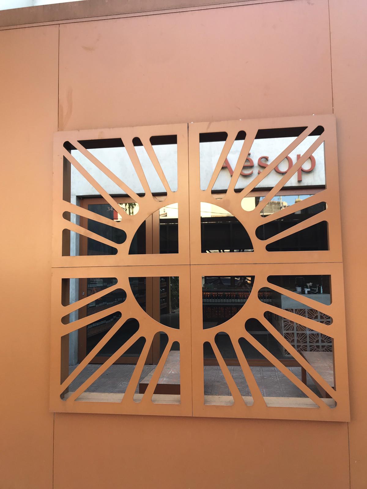 Portão da parte exterior da loja feito em alumínio, pintado do mesmo tom do tijolo e com o símbolo do cobogó no centro dele (Foto: Barbara Cassou)