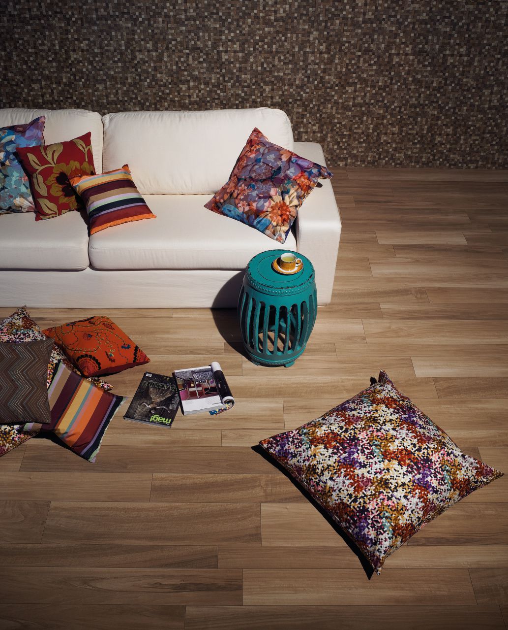 Almofadas em tamanhos diversos e com estampas coloridas contrapõem o estofado branco do sofá 