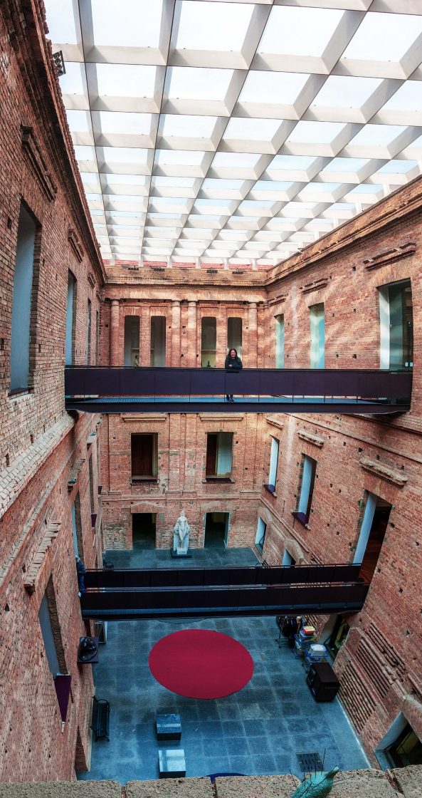Pátio interno da Pinacoteca de São Paulo com paredes de tijolo aparente, passarelas metálicas suspensas e cobertura translúcida em estrutura modular