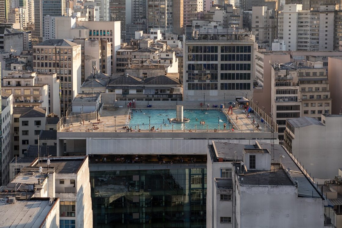 Imagem do Sesc 24 de Maio mostrando piscina no terraço com guarda-corpo de vidro, usuários aproveitando o espaço e edifícios altos ao fundo