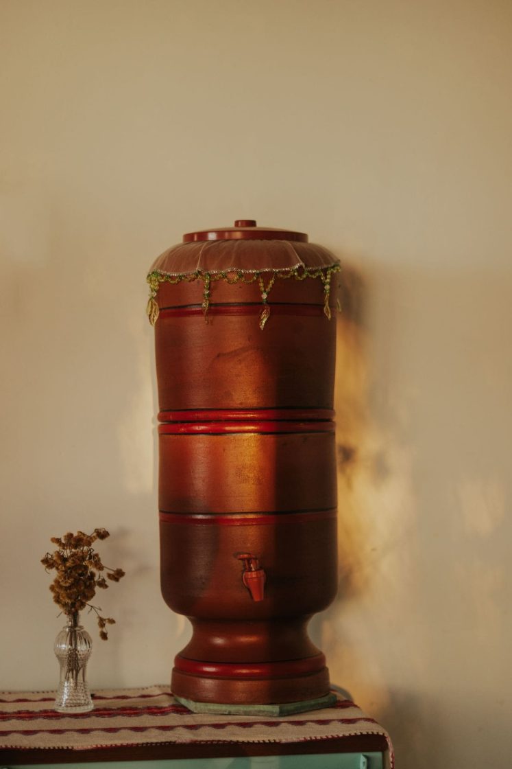 Filtro de barro em destaque sobre mesa decorada com tecidos e elementos rústicos, reforçando a estética acolhedora das festas juninas e das casas de campo