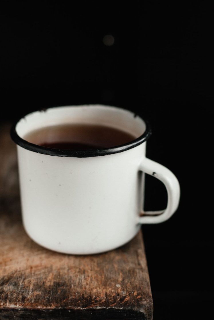 Caneca esmaltada branca apoiada sobre superfície de madeira, elemento tradicional que remete às cozinhas rurais e ao aconchego das festas juninas