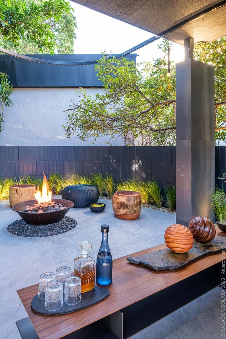 Área externa contemporânea com paisagismo, mobiliário de apoio e fire pit central, alternativa para reproduzir o clima das fogueiras juninas