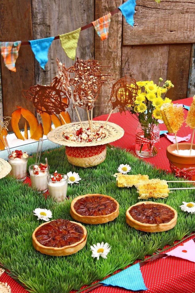 Composição junina com tortas, milho assado, doces, flores e elementos artesanais organizados em uma mesa temática colorida e acolhedora