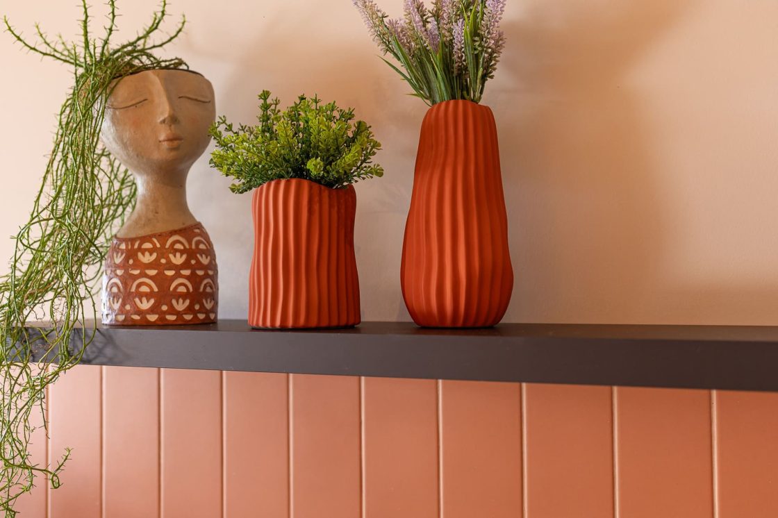 Prateleira decorada com vasos e cachepôs em tons terrosos, plantas ornamentais e parede em paleta quente e acolhedora para ambientes de inspiração rústica e natural
