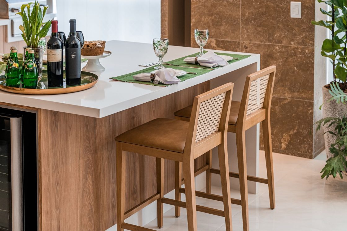 Ilha de cozinha com duas banquetas e mesa posta com jogo americano, taças, pratos e guardanapos