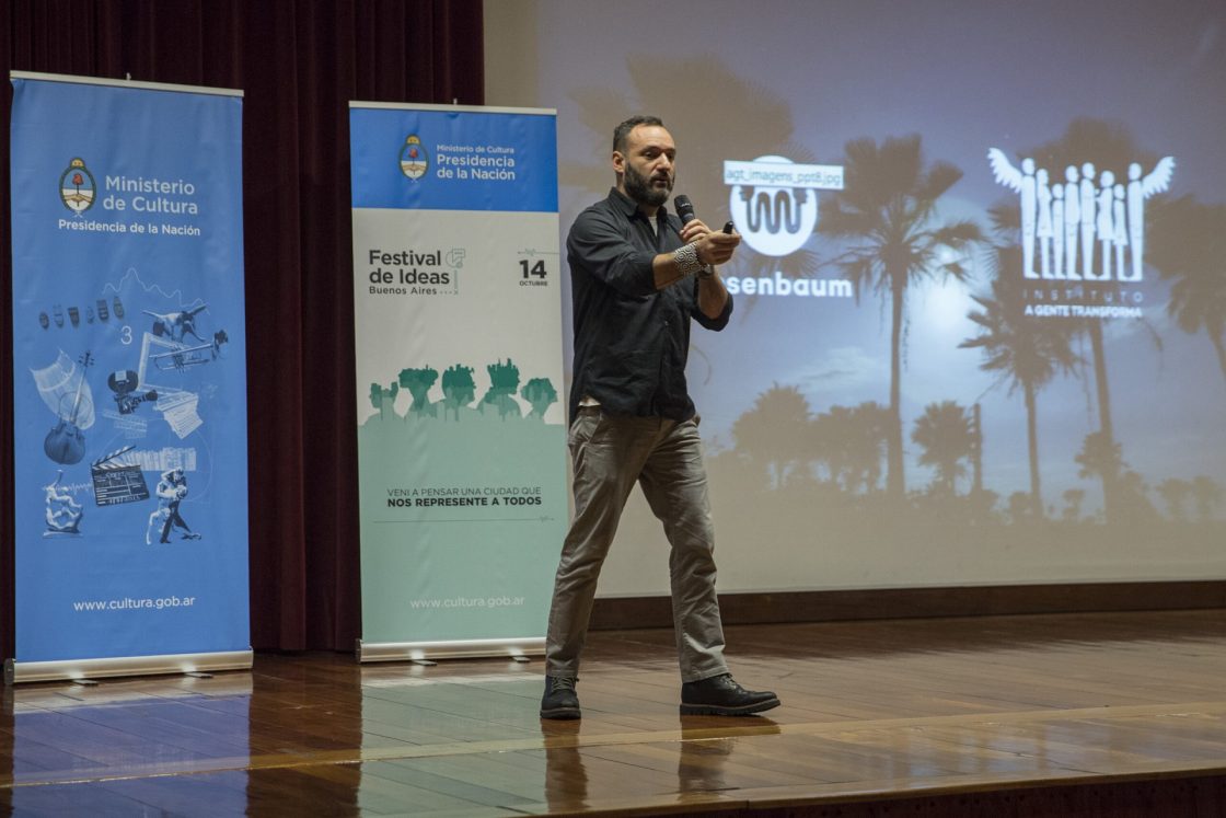 Marcelo Rosenbaum em palco, segurando microfone enquanto dá palestra
