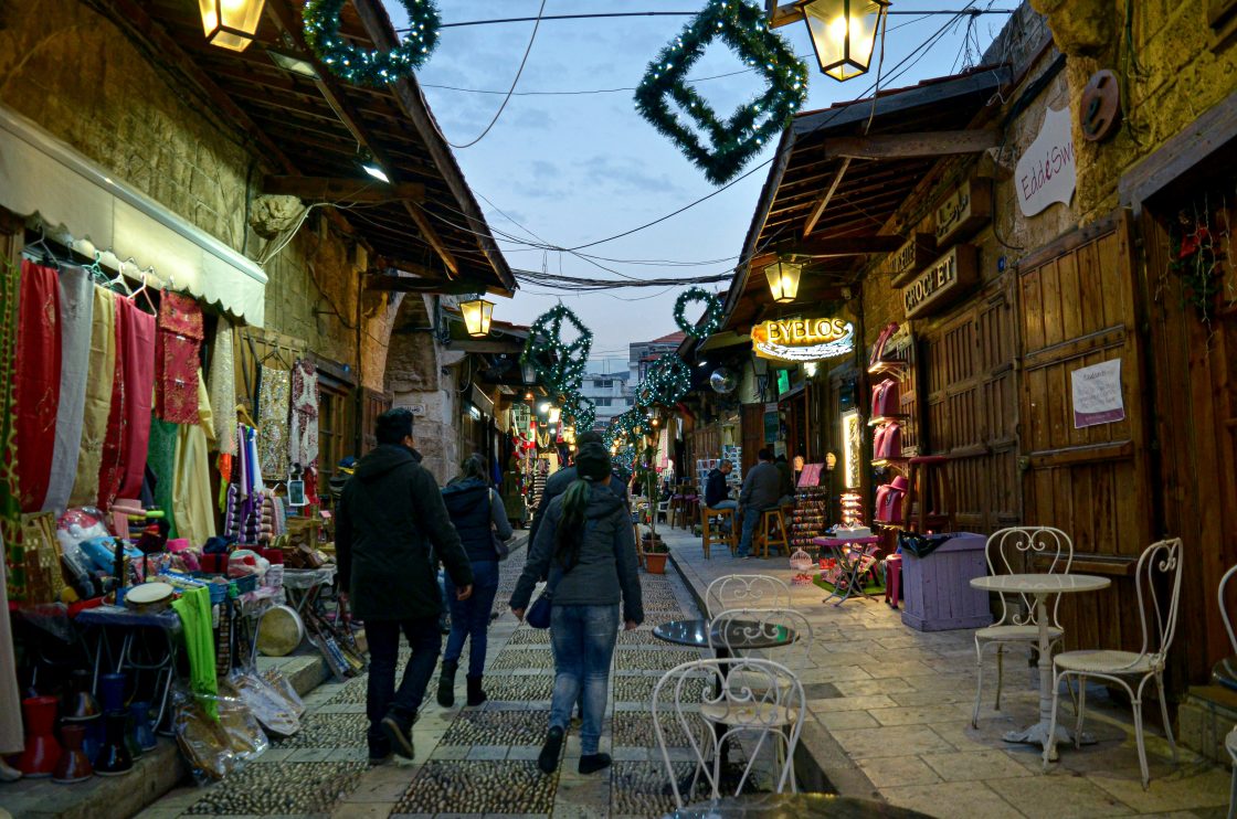 A group of people walking down a street next to shops Byblos, Lebanon