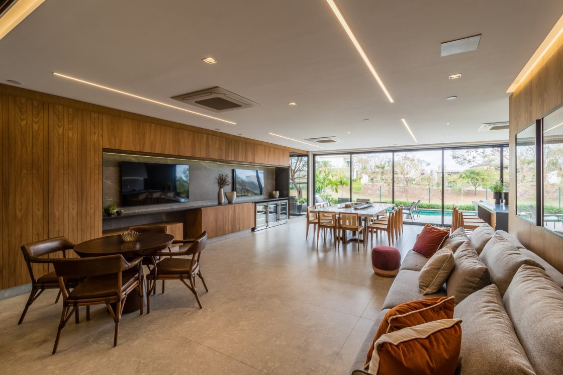 Sala ampla com parede ripada com televisão, piso e rodapé em porcelanato que reproduz pedra