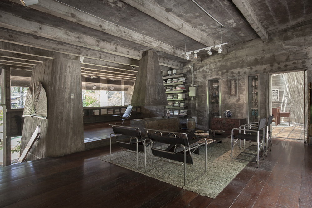 Casa em concreto aparente tem vigas e tubulações à mostra, em um estilo que se assemelha ao industrial