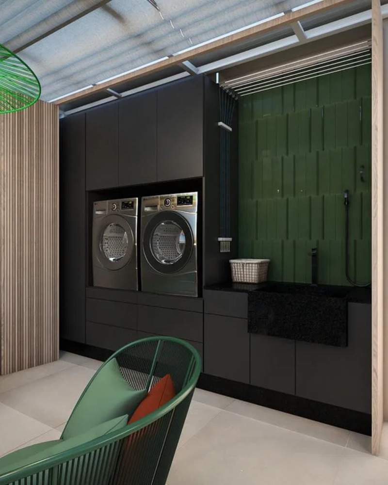 ambiente para área de lavar, com móveis pretos e pia preta, duas máquinas de lavar embutida no armário, sofá com tiras abertas na tonalidade verde escuro e uma pia grande escura