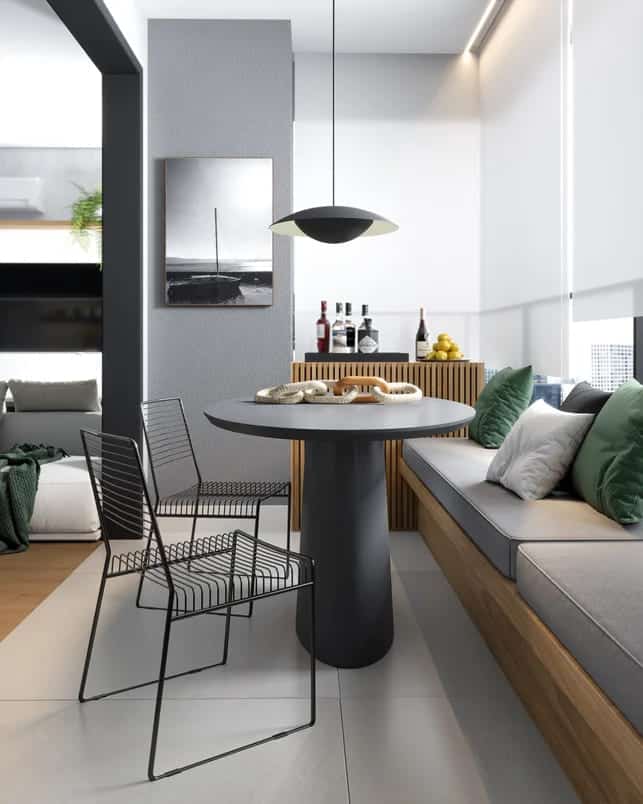 Área de lazer interna, com móveis modernos em tons cinza e preto. Mesa redonda para jantar acoplada com sofá e cadeiras