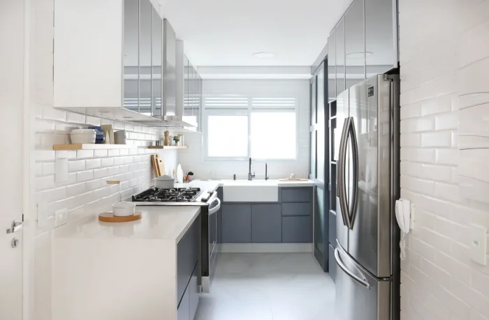 Cozinha estreita, com fogão e geladeira cinza, detalhe em tijolos brancos na parede, prateleiras suspensas 