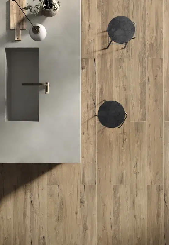 Visão superior de bancada cinza e duas banquetas. O piso da cozinha é feito de revestimento que interpreta madeira.
