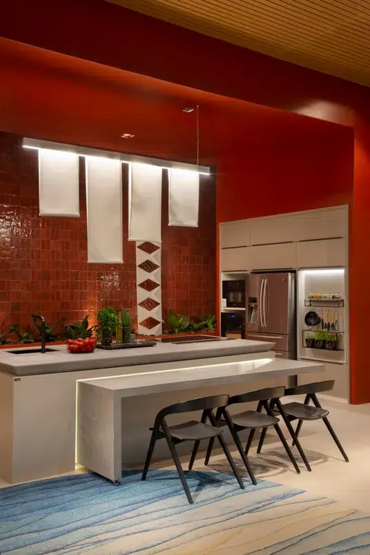 Cozinha com paredes vermelhas, com ilha central e uma bancada rebaixada com três cadeiras. Projeto com estilo oriental e móveis minimalistas.