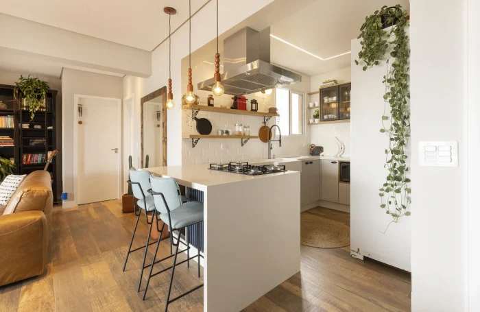Cozinha com paredes e bancada americana branca, piso com aparência de madeira e ambiente integrado à sala.