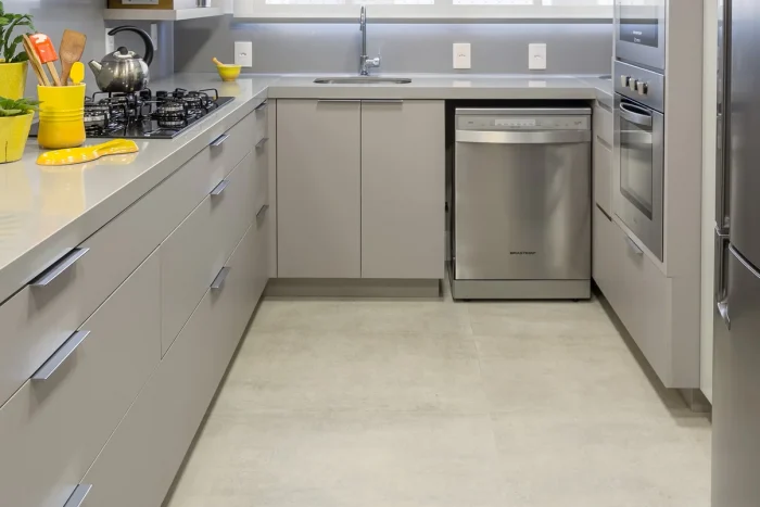 Cozinha planejada, com armário cinza claro, geladeira, máquina de lavar e microondas. Bancada lisa claro e chão de porcelanato