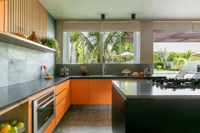 Cozinha integrada com área externa, bancada em L ampla em tons de madeira e cooktop preto na ilha central 