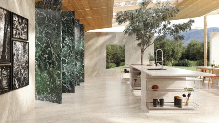 Cozinha ampla, com área aberta, plantas verdes, parede em mármore com tons de verde e bancada de cozinha retangular grande em porcelanato 