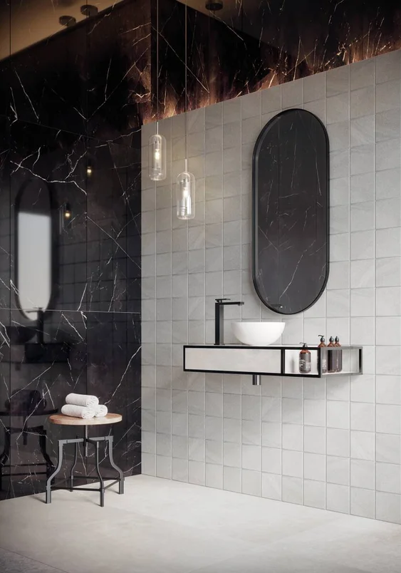 Banheiro moderno com banco baixo abrigando três toalhas de rosto. Pia com cuba redonda e torneira quadrada preta, espelho preto e decoração toda em preto e branco