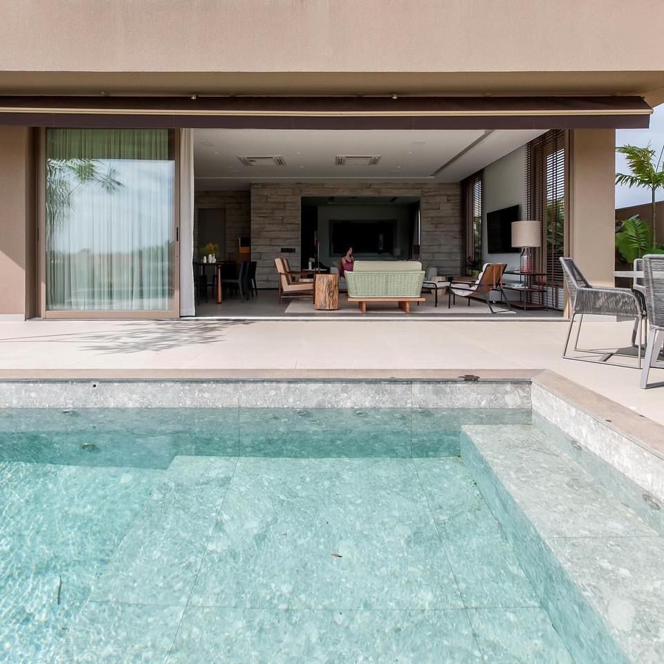 Área externa integrada ao interior da casa. Na piscina, revestimento de porcelanato que reproduz pedra