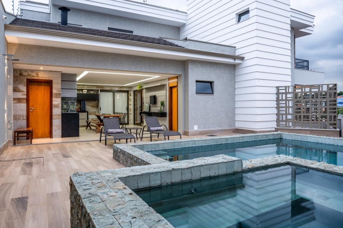 Piscina com revestimento em pedra natural em área externa com piso em porcelanato amadeirado