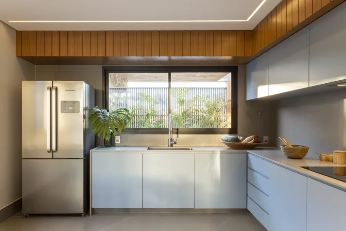 Cozinha com móveis bancos, geladeira inox com portas duplas e detalhes em madeira no teto