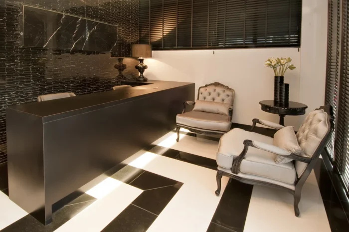 Sala de espera com pisos pretos e branco, poltronas no estilo clássico e bancada preta.