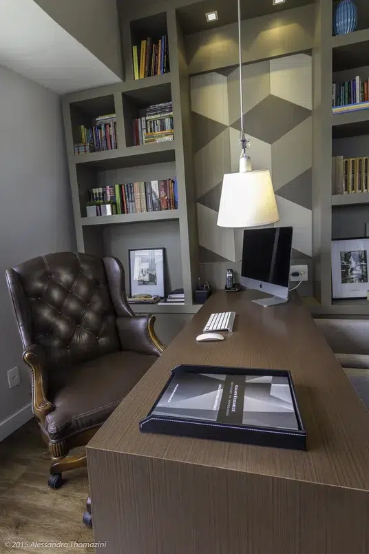 Mesa de um escritório com poltrona marrom e ao fundo uma estante de livros