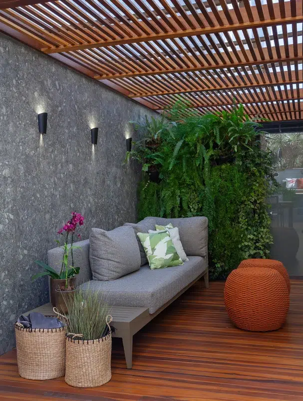 Jardim de inverno com sofá cinza, vasos de plantas e piso em madeira
