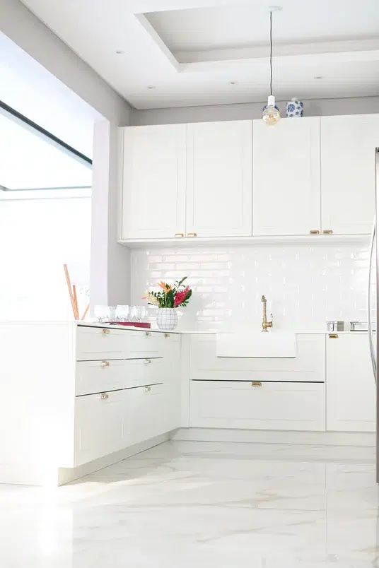 Cozinha com peças brancas, piso marmorizado, armários com gavetas amplas e um vaso de flores
