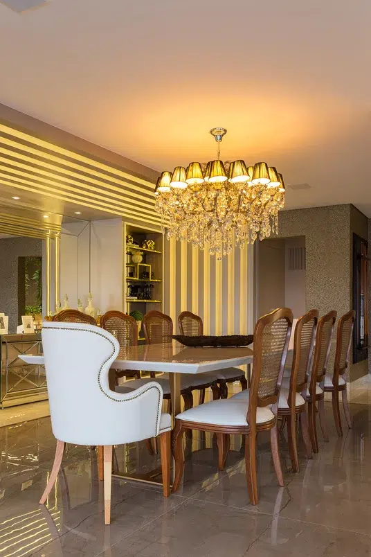 Sala de jantar no estilo clássico com cadeiras adornadas, lustre e muitos pontos de iluminação