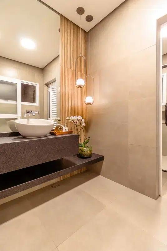 Banheiro em tons de marrom com bancada de granito e painel ripado de madeira