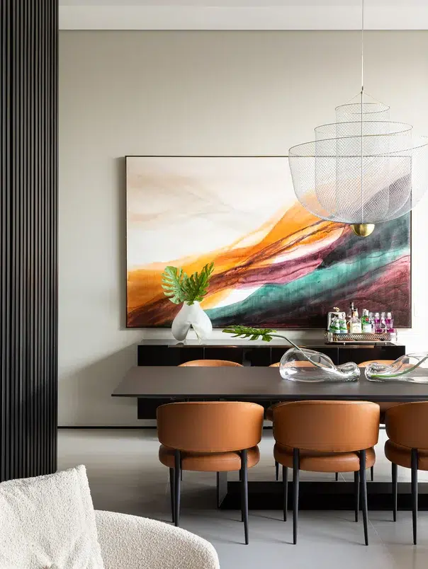 Sala de jantar com mesa preta, cadeiras de couro marrom, adereços de vidro acima do tampo e quadro colorido na parede do fundo