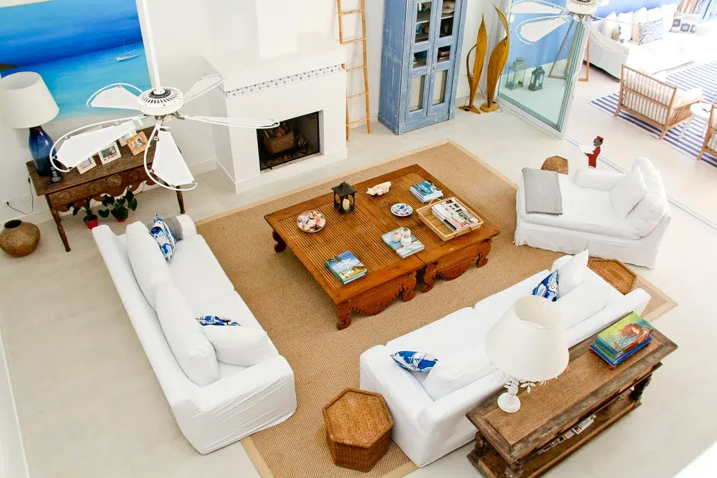 Sala de estar com decoração praiana, móveis em madeira, sofás brancos e detalhes em azul