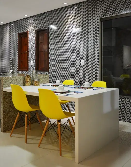 Cozinha com parede do fundo revestida com o Cobogó Indigo da Linha Vila Madá e cadeiras amarelas na mesa branca.