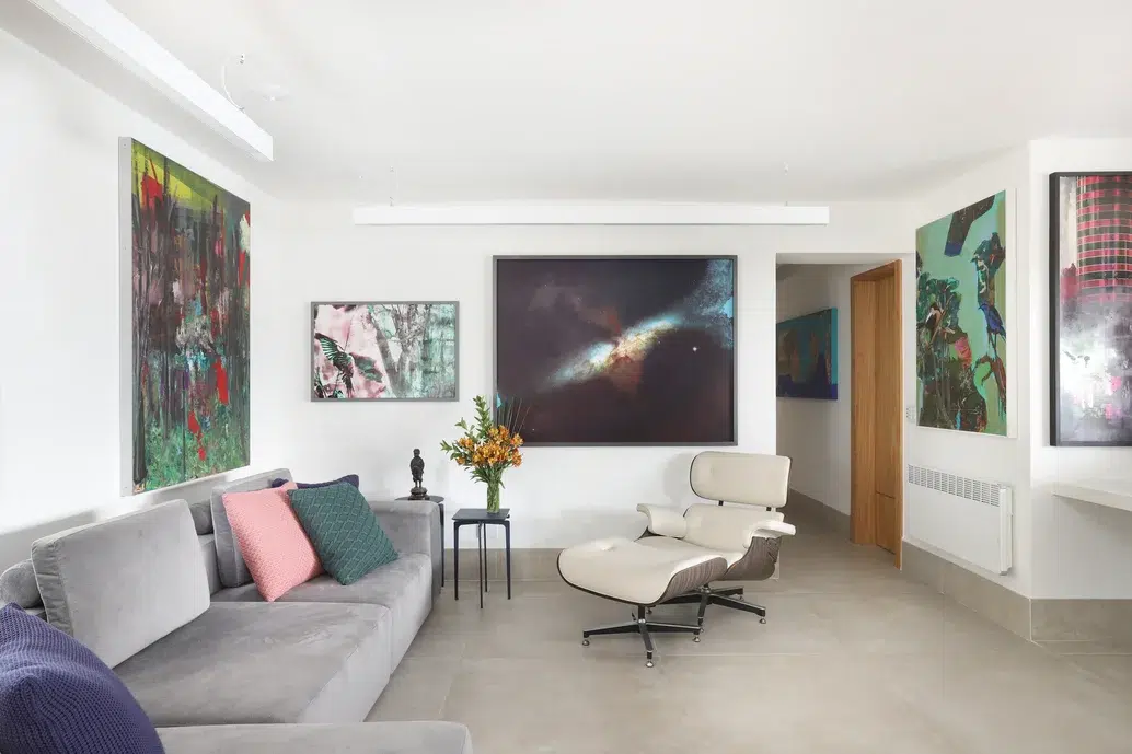 Sala de estar de um apartamento com um sofá de cor cinza e almofadas de cores. Quadros grandes com diferentes cores em todas as paredes.