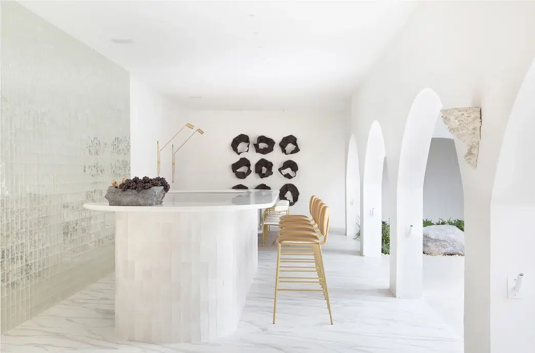 Área externa de mármore branco e mesa branca com banquetas em cor bege. 