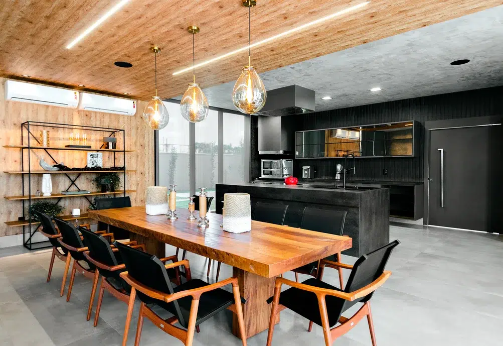 Sala e cozinha de uma casa estilo industrial com mesa de madeira natural e lampadas estilo industrial. Cores preto e madeira. 