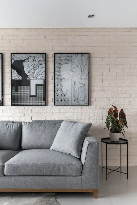 Metade de um sofá cinza, com uma decoração de planta do lado e quadros em preto e branco na parede atrás do sofá.