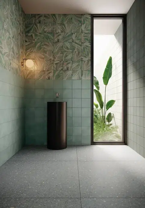 banheiro com meia parede em tons de branco, verdes e toques de tons terrosos e outras cores que fazem um visual de folhas verdes.