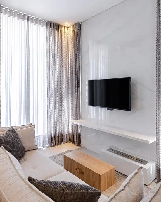 Sala de estar de um apartamento pequeno em cores claras, TV na parede branca de frente ao sofá.