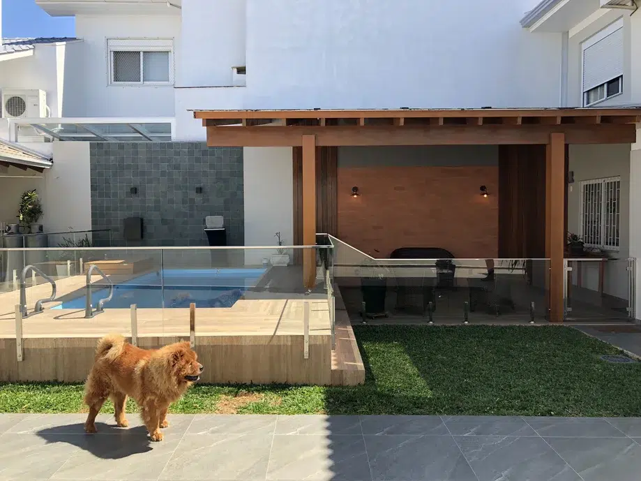 Área externa de uma casa com piscina com deque e um cachorrinho.