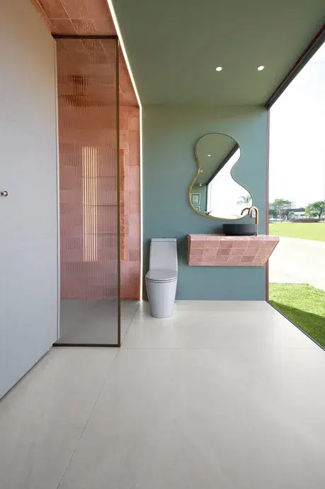 Banheiro de criança com parede azul-petróleo e um espelho irregular com uma pia e box em cor rosa pastel.